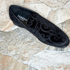 Puede incluir: Mocas&iacute;n de terciopelo negro con un dise&ntilde;o ornamental y ondulado. El zapato presenta un tac&oacute;n bajo y el texto "TERRONI DESIGN" en el interior. Un calzado elegante.