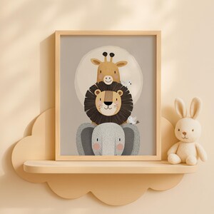 May include: A framed print of a cartoon animal stack: an elephant, a lion, and a giraffe. The animals are in soft colours, with a light background and a white circle behind the giraffe. A stuffed bunny sits on a shelf below.