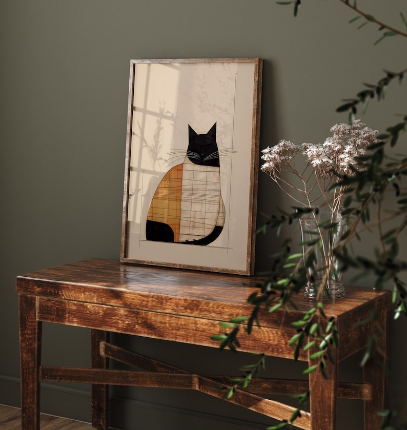 Pu&ograve; includere: Una stampa incorniciata di un'illustrazione geometrica di un gatto nero, bianco e arancione. La stampa &egrave; appesa a un muro sopra un tavolo di legno.