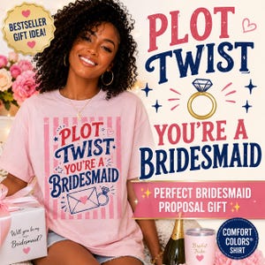 May include: A light pink t-shirt featuring a vertical striped pattern and the text PLOT TWIST YOU'RE A BRIDESMAID in dark blue and red lettering. The design includes a graphic of an envelope and a gold engagement ring icon.