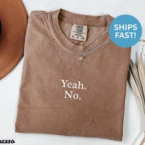 Puede incluir: Camiseta color espresso con el texto "Yeah. No." en blanco. La camiseta tiene cuello redondo y una etiqueta Comfort Colors. Se ve un collar plateado con un pequeño colgante. Un círculo azul con "SHIPS FAST!" está en la parte superior derecha.