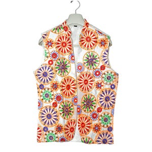 May include: A white sleeveless vest with a colorful floral pattern. The pattern features orange, red, green, blue, and purple flowers on a white background.