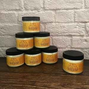 May include: A collection of seven small jars of mineral sunscreen with black lids. Each jar has a label with the words "Mineral Sunblock" and "Made with Tallow and Non-Nano Zinc Oxide". The jars are arranged on a wooden surface.