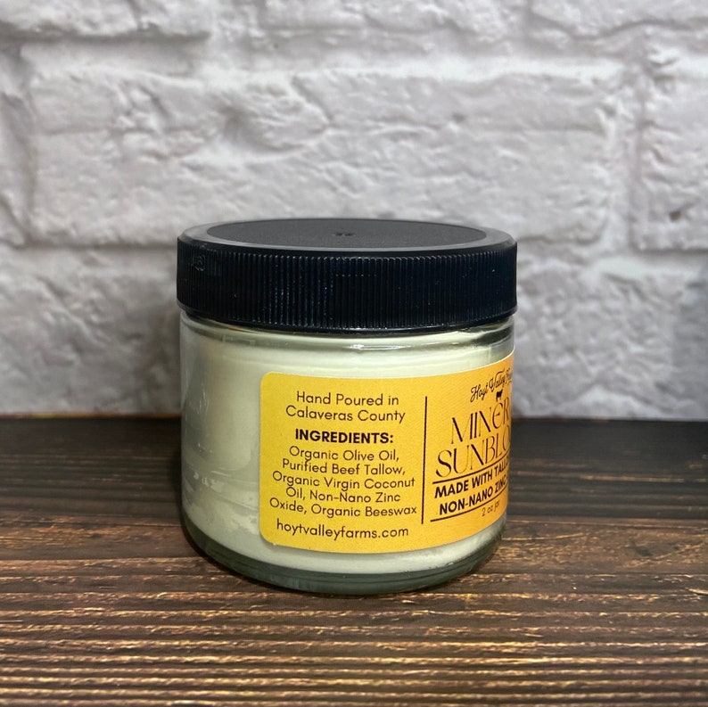 May include: A small glass jar with a black lid, containing a creamy, off-white substance. A yellow label lists ingredients like organic olive oil and beeswax. The text "MINERAL SUNBLOOM" is visible on the label.