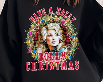 May include: Black sweatshirt with a graphic featuring Dolly Parton. The design includes the text "Have a Holly Dolly Christmas" in red, with a wreath of lights and greenery around her portrait. The background has a plaid pattern.