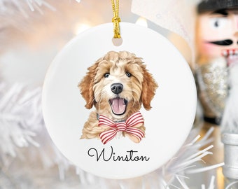 Peut inclure: Une boule de Noël en céramique blanche avec une illustration aquarelle d'un chien brun et blanc portant un nœud papillon rouge et blanc à rayures. Le nom du chien, "Winston", est écrit en cursive noire sous l'illustration.