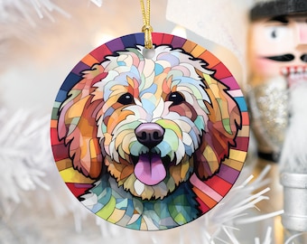 May include: A colorful, abstract, stained glass style Christmas ornament featuring a white dog with brown ears. The dog is smiling with its tongue sticking out. The ornament is round and has a gold string for hanging.