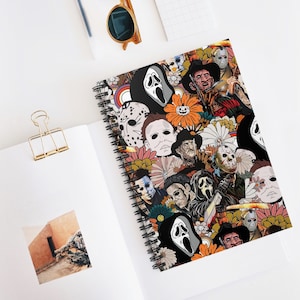 Puede incluir: Cuaderno de espiral con un diseño de portada con personajes de películas de terror y motivos florales. La portada muestra villanos icónicos como Michael Myers, Freddy Krueger y Ghostface, sobre un fondo de flores naranjas y rosas. El cuaderno está abierto sobre una superficie blanca.