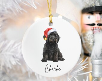 May include: A white ceramic Christmas ornament featuring a black dog wearing a red Santa hat. The dog's name, "Charlie", is written in cursive at the bottom of the ornament.