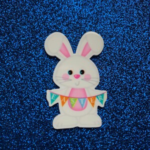 Może przedstawiać: Biały królik trzymający baner z napisem "Easter" w kolorach tęczy. Królik ma różowe uszy i różowy nos. Tło to błyszcząca niebieska powierzchnia.