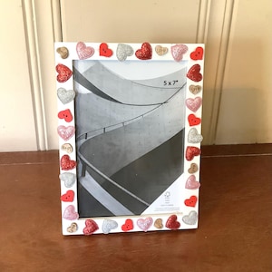 May include: White picture frame decorated with red, silver, and pink glitter hearts, red buttons, and small wooden hearts with the word "Love". The frame is sized 5x7 inches and contains a black and white photo.