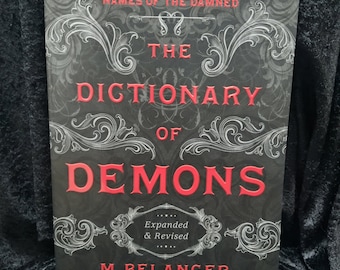 May include: A black book cover with the title "The Dictionary of Demons" in red lettering. The book is an expanded and revised edition by M. Belanger.