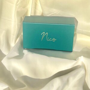 May include: A teal gift box with the name "Nico" written in gold lettering.