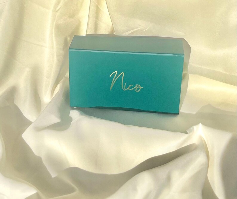 May include: A teal gift box with the name "Nico" written in gold lettering.