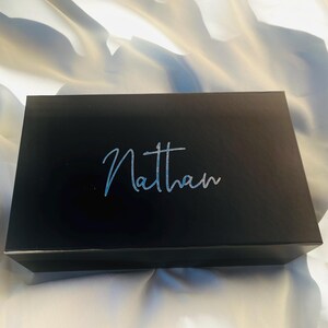 May include: A black gift box with the name "Nathan" written in silver lettering on the top.