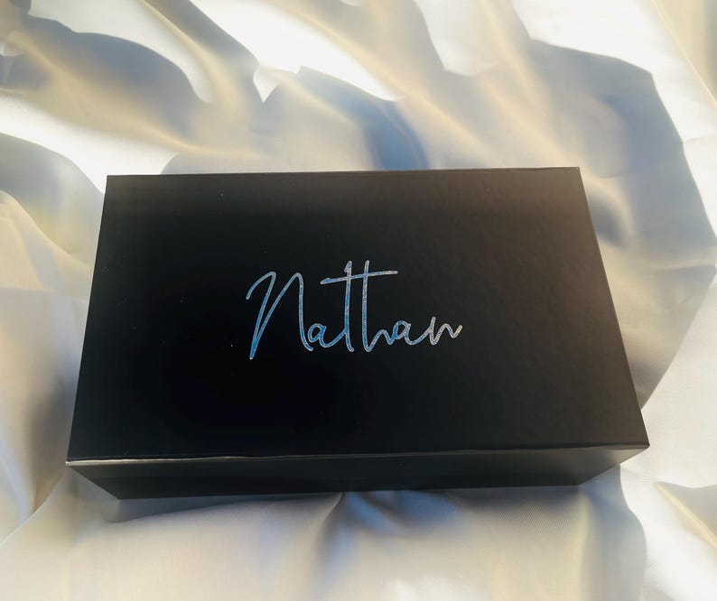 May include: A black gift box with the name "Nathan" written in silver lettering on the top.