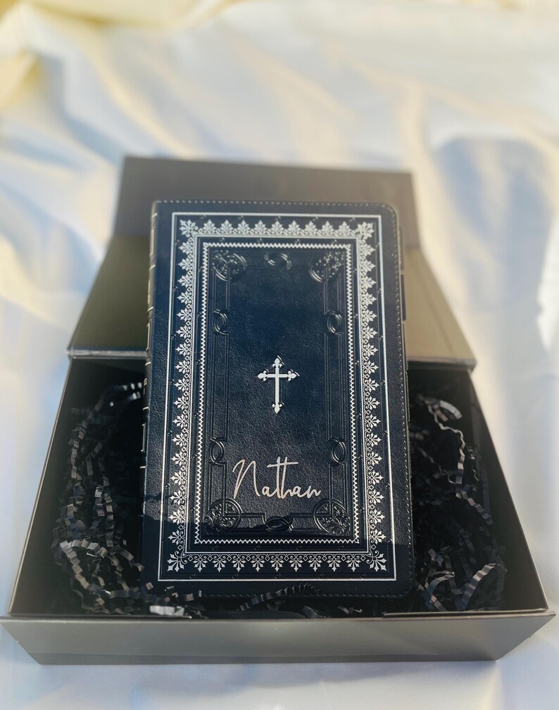 May include: A black leather-bound journal with a silver cross and the name "Nathan" embossed on the front cover. The journal is in a black gift box with black shredded paper.