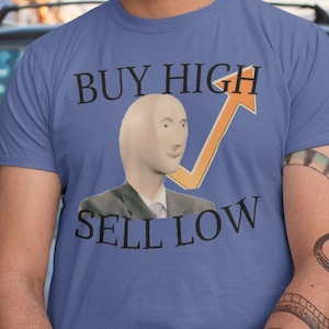Könnte beinhalten: Ein blaues T-Shirt mit einem kahlköpfigen Mann im Anzug und einem gelben Pfeil, der nach oben zeigt. Der Text "BUY HIGH SELL LOW" ist auf das T-Shirt gedruckt.