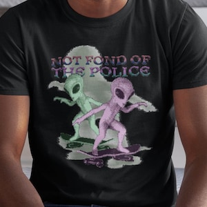 May include: Black t-shirt with a graphic of two green and pink aliens skateboarding. The text "NOT FOND OF THE POLICE" is printed above the aliens.