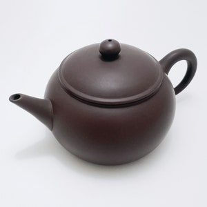 May include: A dark brown ceramic teapot with a round body and a lid with a small knob on top. The teapot has a spout and a handle.