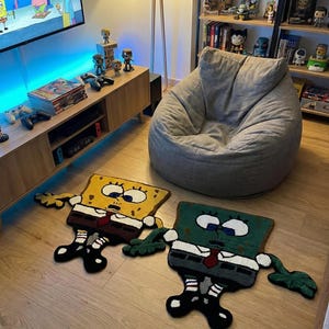 May include: Two cartoon character rugs, one yellow and one green, are on a wooden floor. The yellow rug depicts a character with a brown tie and black shoes. The green rug shows a similar character with a red tie and black shoes. A grey beanbag chair is in the background.