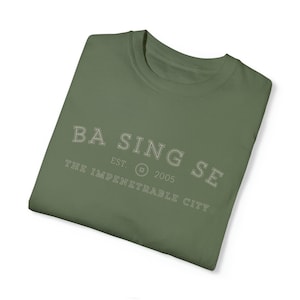 Pode incluir: Uma camiseta verde com o texto "Basing Se" em branco, com as palavras "EST. 2005" e "The Impenetrable City" abaixo.