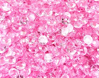 May include: A close-up image of a large quantity of pink iridescent rhinestones. The rhinestones are scattered randomly and appear to be made of glass or plastic.