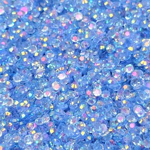 May include: A close-up image of a large quantity of small, iridescent blue rhinestones. The rhinestones are scattered randomly and appear to be made of glass or plastic.