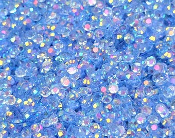 Pode incluir: Uma imagem de close-up de uma grande quantidade de pequenos strass azuis iridescentes. Os strass estão espalhados aleatoriamente e parecem ser feitos de vidro ou plástico.