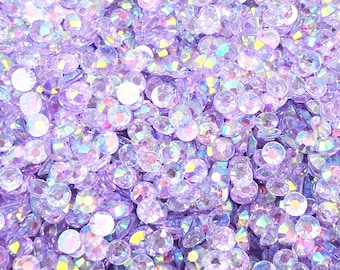 May include: A close-up image of a large quantity of iridescent purple rhinestones. The rhinestones are small and round, and they have a shiny, reflective surface.