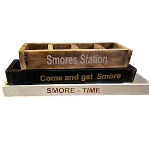 Könnte beinhalten: Drei Holztabletts übereinander gestapelt. Das obere Tablett ist braun mit der Aufschrift "Smores Station". Das mittlere Tablett ist schwarz mit "Come and get S'more". Das untere Tablett ist weiß mit "SMORE - TIME".