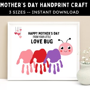 Op de afbeelding: Een ingelijste Moederdag handafdruk knutsel met de tekst "HAPPY MOTHER'S DAY FROM YOUR LITTLE LOVE BUG". Het ontwerp toont drie handafdrukken in roze, rood en paars, die een rups vormen met een cartoon keverkop.