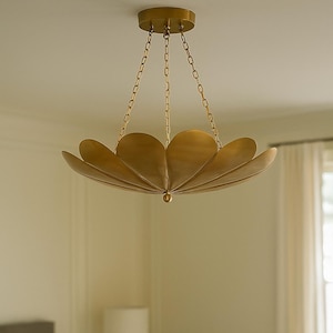 May include: A gold-coloured, petal-shaped chandelier hangs from the ceiling. The light fixture is suspended by gold chains and features a central sphere. The room has a neutral colour palette with a bedside table and lamp visible.