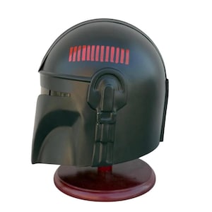 May include: A dark green helmet with a visor and a series of red rectangular lights on top. The helmet is displayed on a dark brown wooden stand. The helmet has a smooth, matte finish.