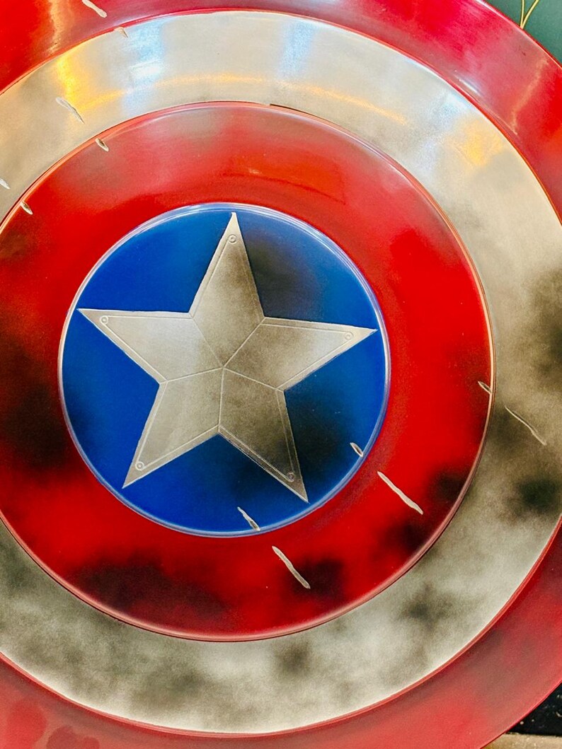 Puede incluir: Primer plano de un escudo con una combinaci&oacute;n de colores rojo, blanco y azul. El escudo presenta un c&iacute;rculo azul central con una estrella plateada. Los anillos exteriores son rojos y plateados, con una apariencia desgastada y envejecida.