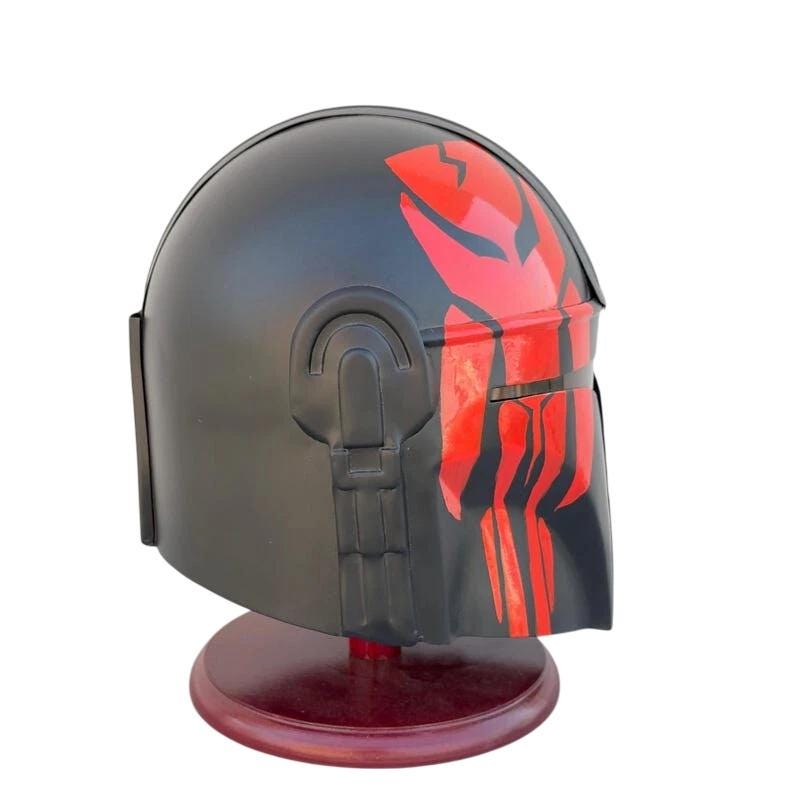 May include: Black helmet with red accents, displayed on a wooden stand. The helmet features a distinctive red design on the front and top. The helmet is a replica of a character's helmet from a science fiction franchise.