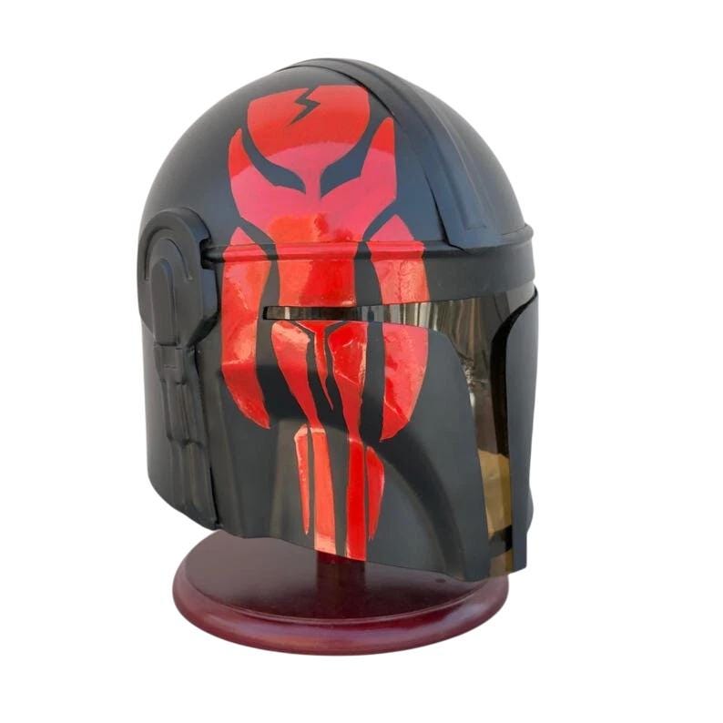 May include: A black helmet with red accents, displayed on a wooden stand. The helmet features a red lightning bolt design on the top and a stylized face design on the front. The visor is dark, and the helmet is angled to the side.