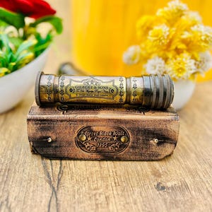 May include: A vintage brass telescope with the text "GILBERT & SONS" and "Street Black Walt London 1895" on a brown leather case. The telescope is cylindrical and rests on a rectangular case with decorative details.