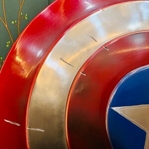 Puede incluir: Primer plano de un escudo del Capit&aacute;n Am&eacute;rica. El escudo presenta c&iacute;rculos conc&eacute;ntricos rojos, plateados y azules. Una estrella blanca est&aacute; centrada en la parte azul. El escudo tiene un acabado brillante y parece ser de metal.