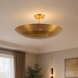 May include: A gold-coloured, bowl-shaped ceiling light fitting with a perforated design. The light is suspended from the ceiling by a central rod. The fitting is illuminated, casting a warm glow.
