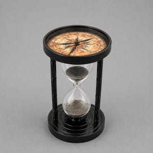 May include: A black hourglass featuring a clear glass bulb filled with dark sand, supported by four vertical pillars and a circular base. The top of the frame incorporates a compass dial with a tan, aged-look background and black directional markings.