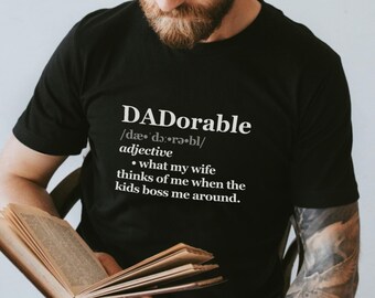Peut inclure: Un t-shirt noir avec du texte blanc qui dit "DADorable /dæ dǝrǝbl/ adjectif • ce que ma femme pense de moi quand les enfants me donnent des ordres."
