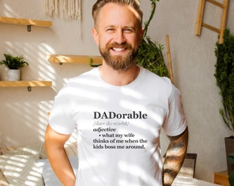 Peut inclure: T-shirt blanc avec une définition humoristique du mot "DADorable" imprimée sur le devant. La définition se lit comme suit : "ce que ma femme pense de moi quand les enfants me donnent des ordres."