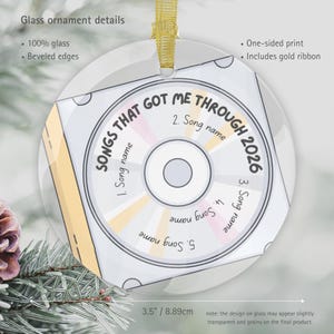 May include: A round glass ornament with beveled edges and a gold ribbon. The design features a compact disc graphic with the text "SONGS THAT GOT ME THROUGH 2026" and five numbered lines for song names. The ornament measures 3.5 inches in diameter.
