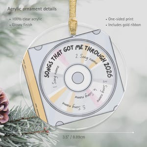 May include: A round clear acrylic ornament with a glossy finish, measuring 3.5 inches in diameter. It features a graphic of a CD with the text SONGS THAT GOT ME THROUGH 2026 and five numbered song name slots. It includes a gold ribbon for hanging.