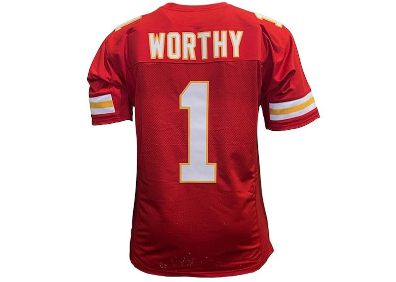 May include: Red football jersey with the name "WORTHY" and the number "1" in white and gold. The jersey has white and gold stripes on the sleeves and shoulders. The jersey is made of a mesh material.