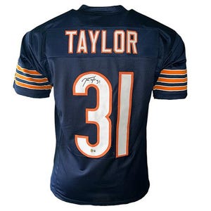 May include: Navy blue football jersey with the name "TAYLOR" across the shoulders and the number "31" on the back. The jersey has orange and white accents and a signature.