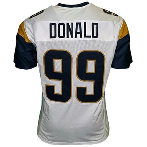 May include: White football jersey with navy blue and gold accents. The jersey features the name "DONALD" across the upper back and the number "99" in navy blue with gold trim. The sleeves are navy blue.