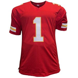 May include: A red football jersey with the number 1 in white and a yellow outline. The jersey has a V-neck and yellow and white stripes on the sleeves. The jersey is made of a mesh material.