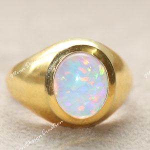 May include: A gold ring featuring an oval opal gemstone. The opal exhibits a play of colour with iridescent shades of blue, green, and pink. The ring has a smooth, polished finish.